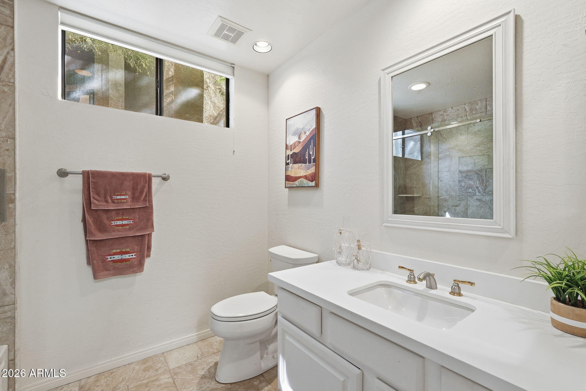 Bathroom with a white vanity, beige tile, and a glass shower reflected in a large mirror.