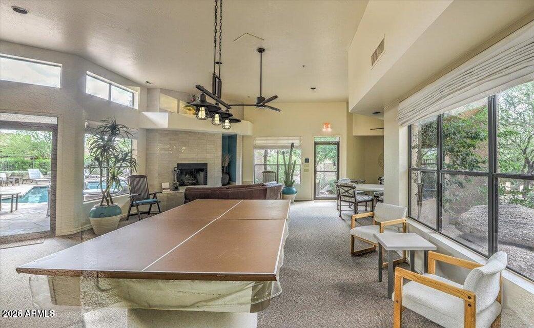 Recreation room with a ping-pong table, fireplace, and windows overlooking a swimming pool.