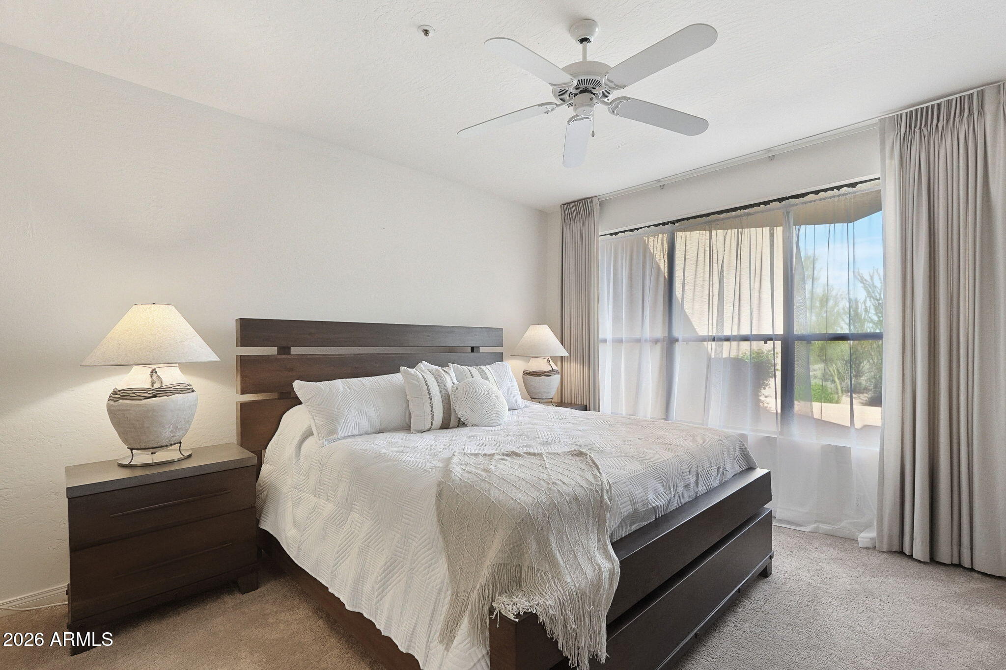 Furnished bedroom with a dark wood bed, white bedding, ceiling fan, and large sliding glass doors.