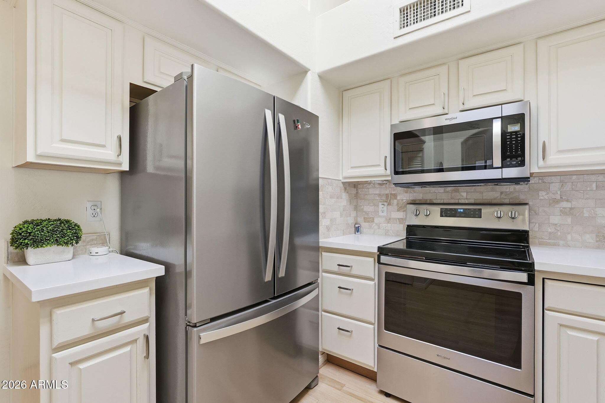 Kitchen with white cabinets, pale tile backsplash, and stainless steel appliances.