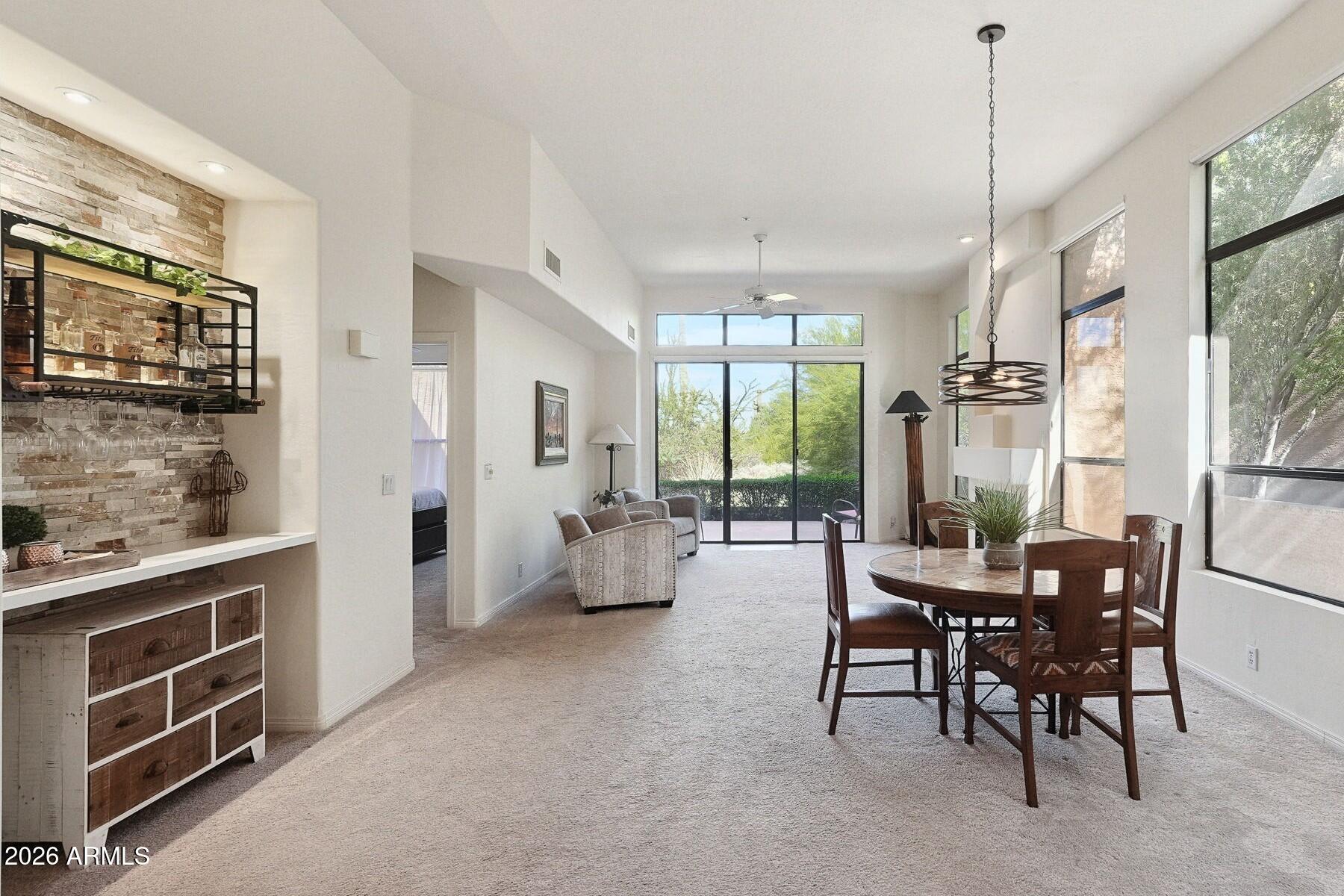 Open-plan living and dining room with a stone accent wall and tall windows overlooking greenery.