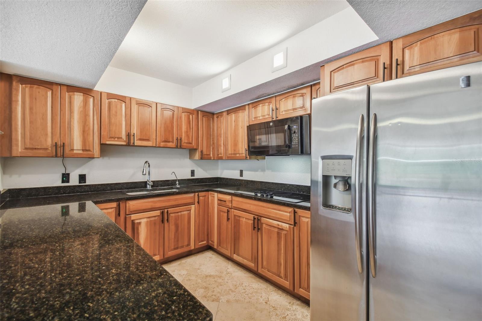 Kitchen with warm wood cabinets, dark stone counters, and stainless steel appliances.