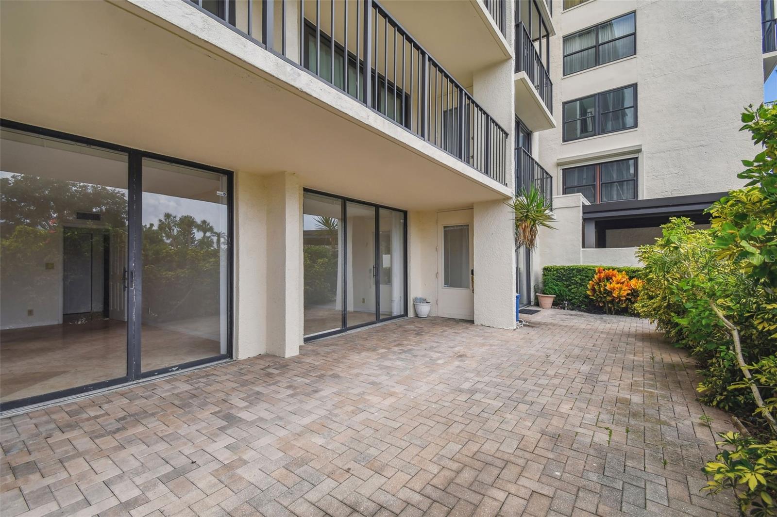 Condominium courtyard patio with brick pavers, sliding glass doors, and balconies above.