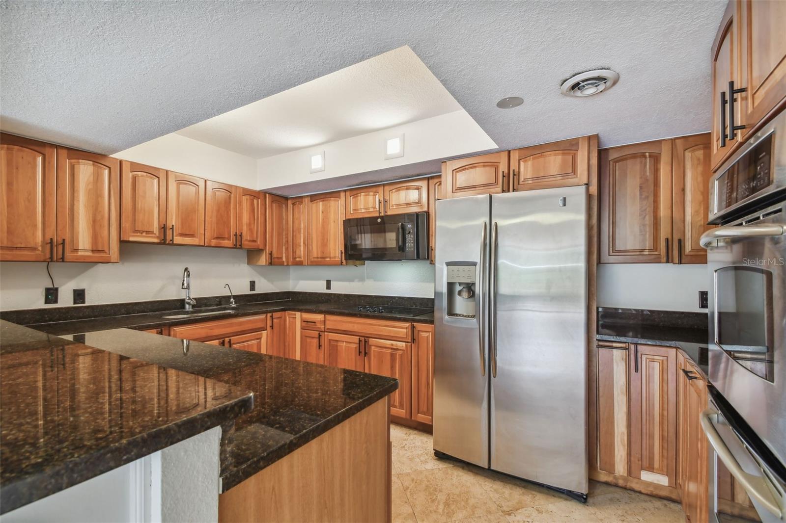 Kitchen with honey-colored cabinets, dark stone counters, and stainless steel appliances.