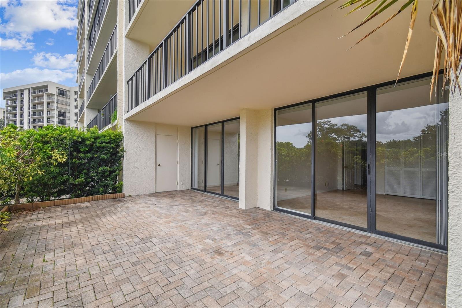 Ground-floor condo patio with brick pavers, sliding glass doors, and a private hedge.