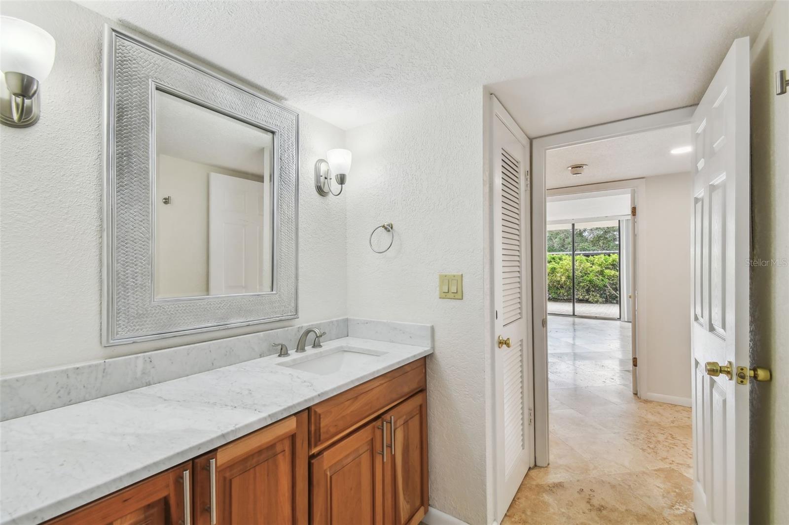 Bathroom vanity with a marble countertop and wood cabinets, opening to a bright adjoining room.