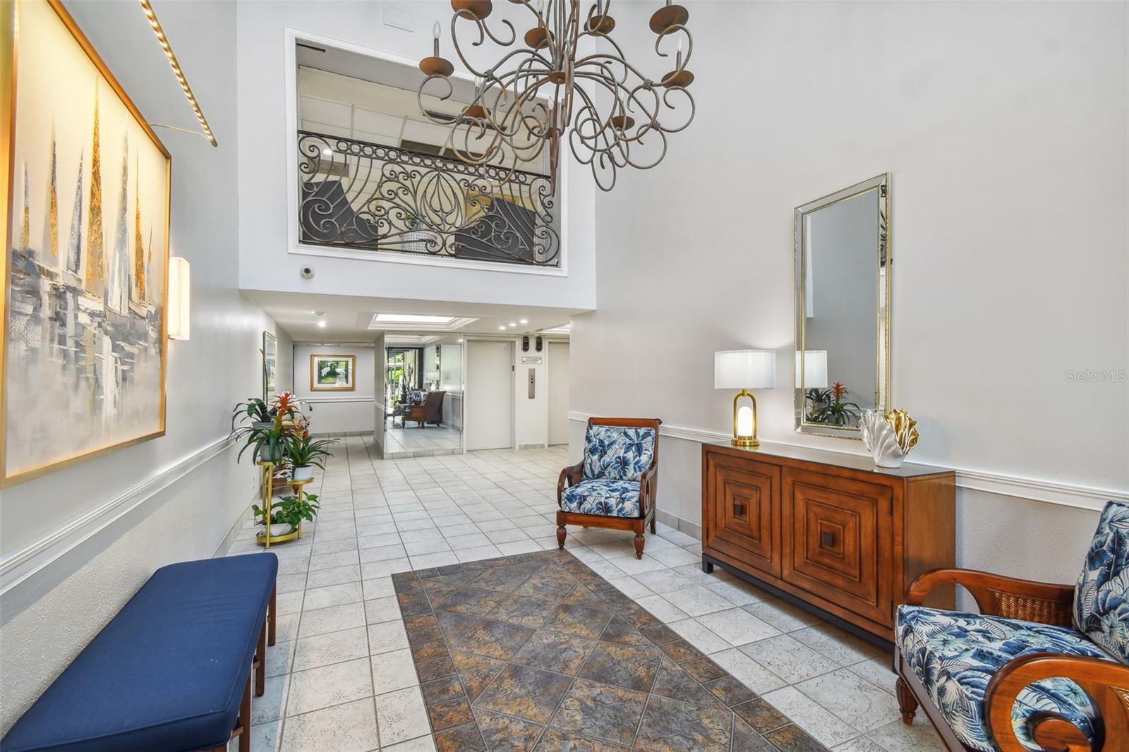 Condominium lobby with a wrought-iron balcony railing, chandelier, tiled floor, and seating.