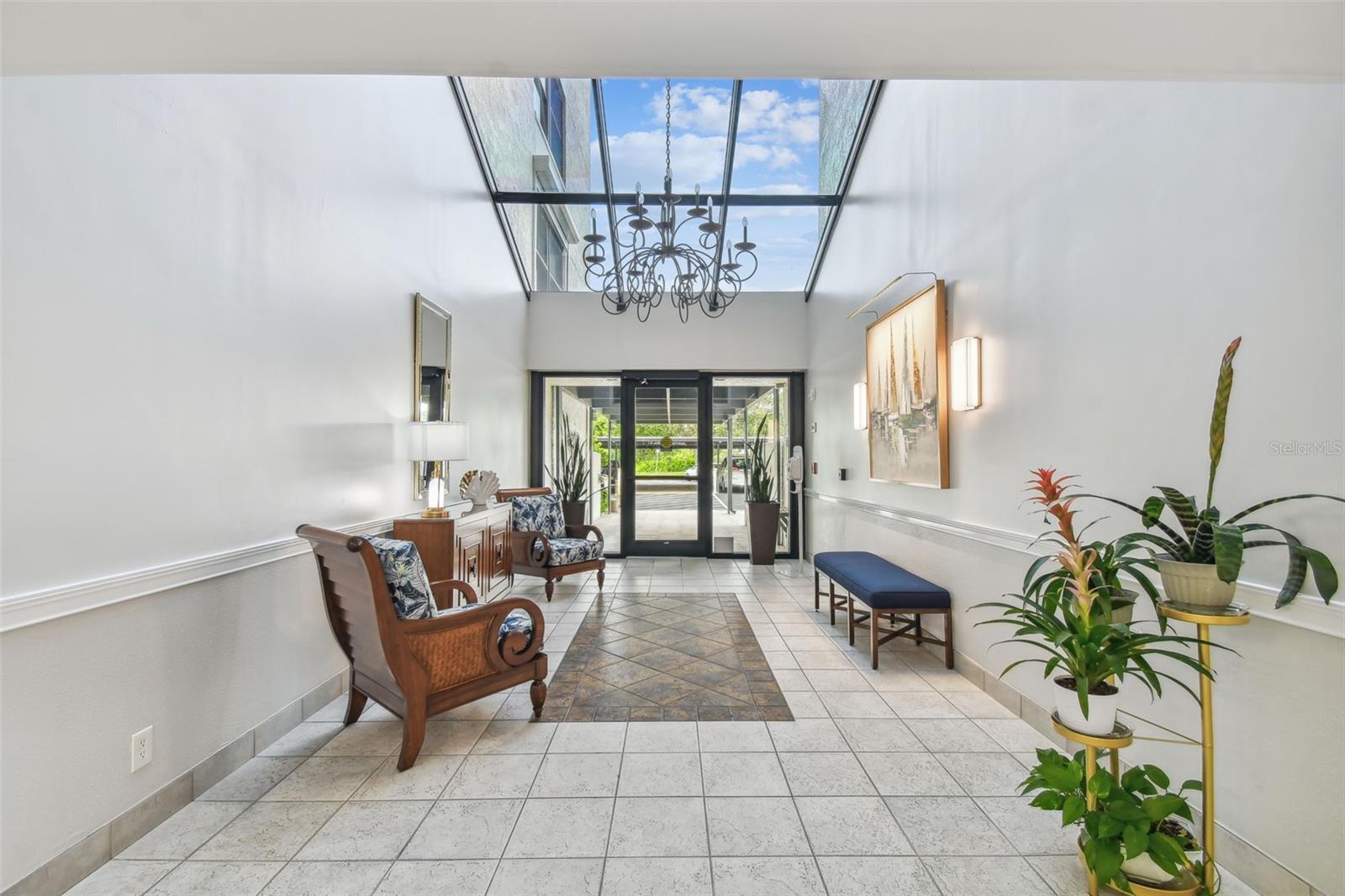 Condominium lobby with a glass skylight, chandelier, tiled floor, and seating area.