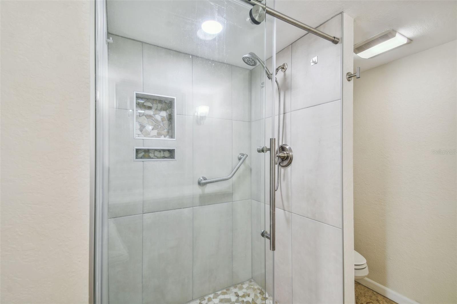 Walk-in shower with glass enclosure, mosaic niches, and a grab bar.