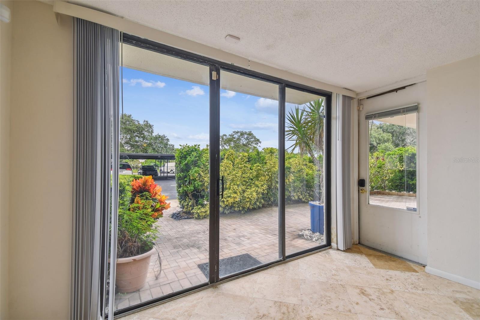 Empty tiled room with sliding glass doors opening onto a landscaped patio.