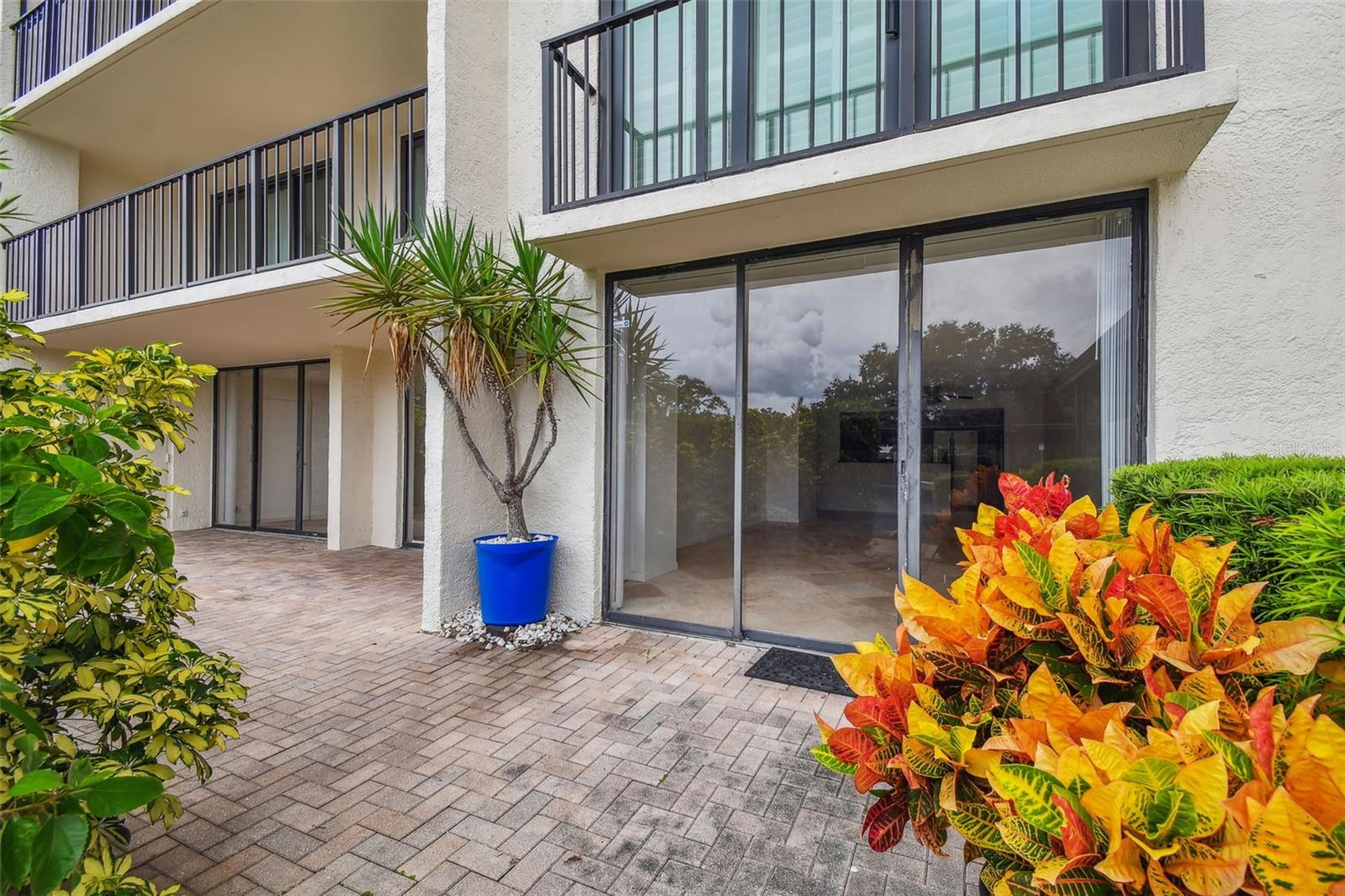 Condominium patio with sliding glass doors, brick pavers, and a blue potted palm.