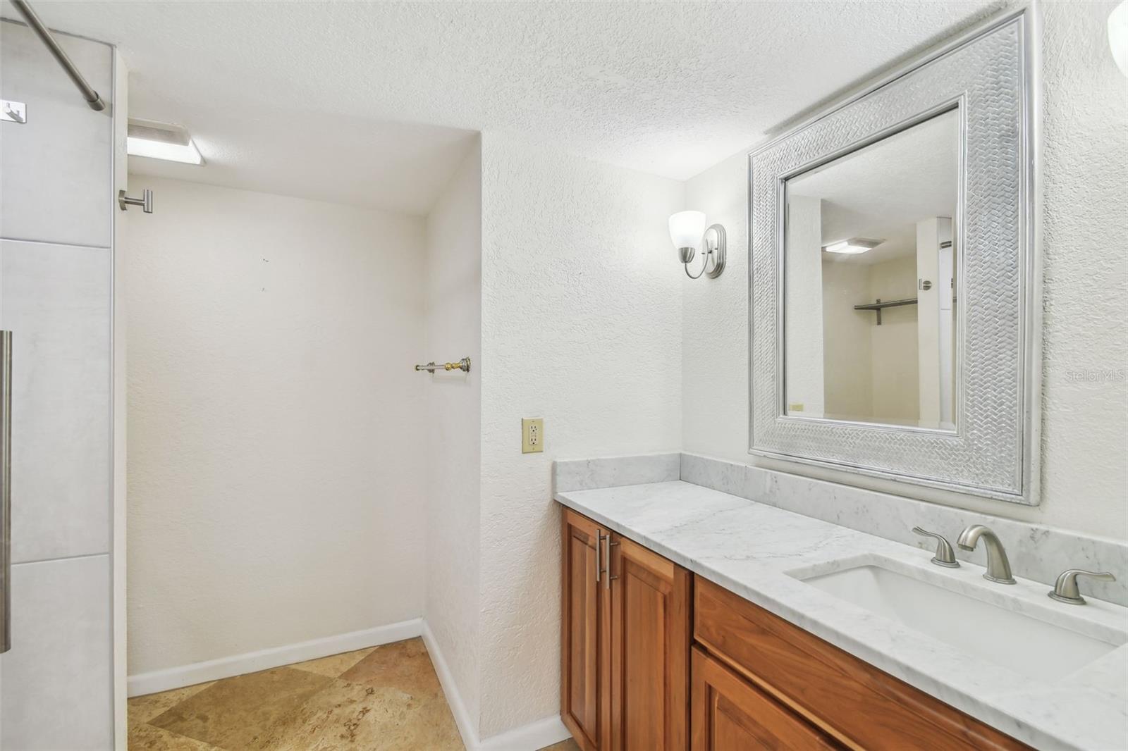 Bathroom vanity with a marble countertop, wood cabinets, and a large framed mirror.