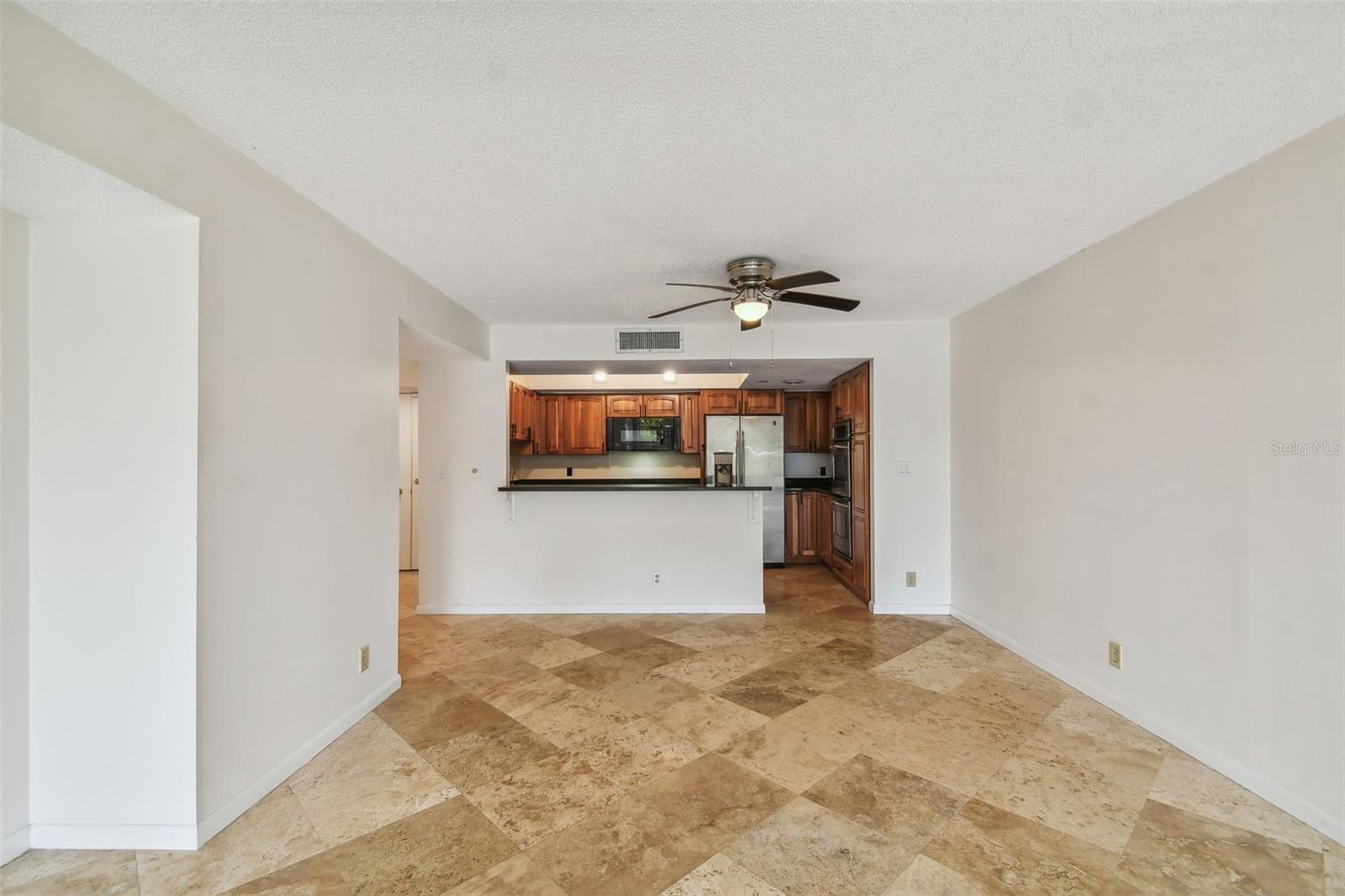 Empty living area with patterned tile flooring and a pass-through to the wood-cabinet kitchen.