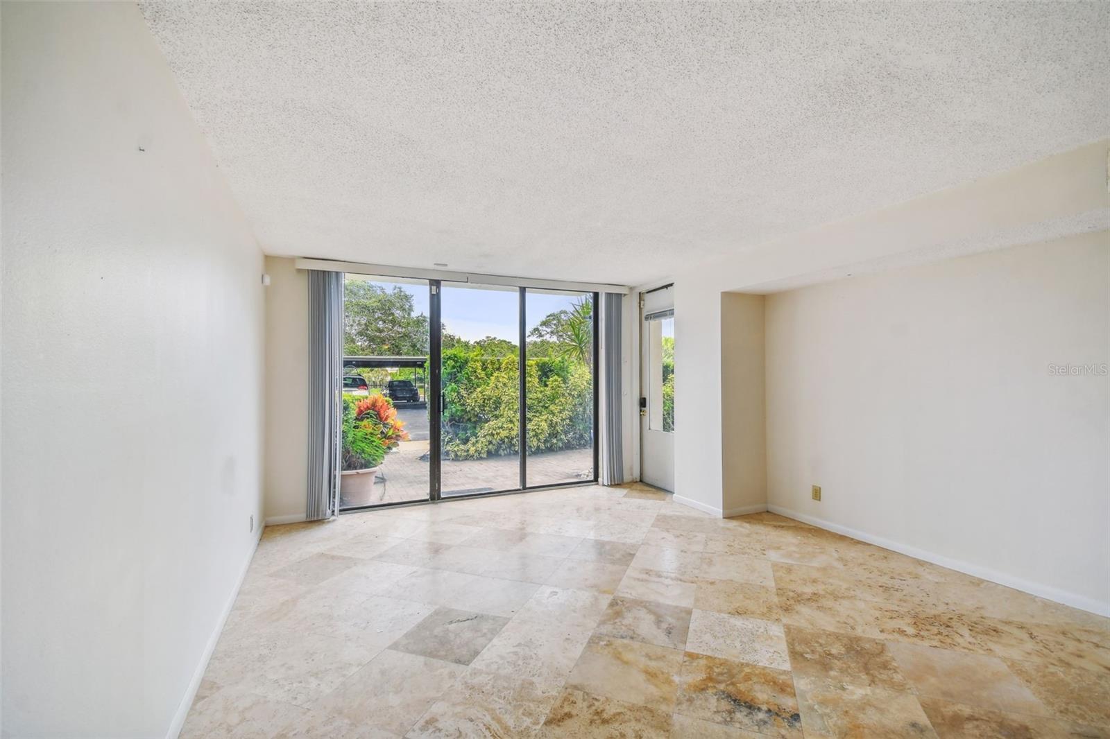 Empty living room with stone tile floors and sliding glass doors opening to a leafy patio.