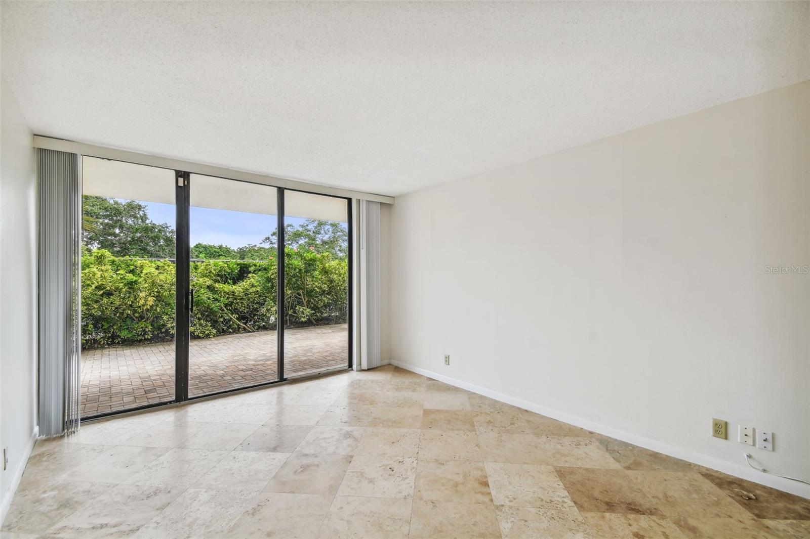 Vacant living room with stone tile flooring and sliding glass doors opening to a paved patio.