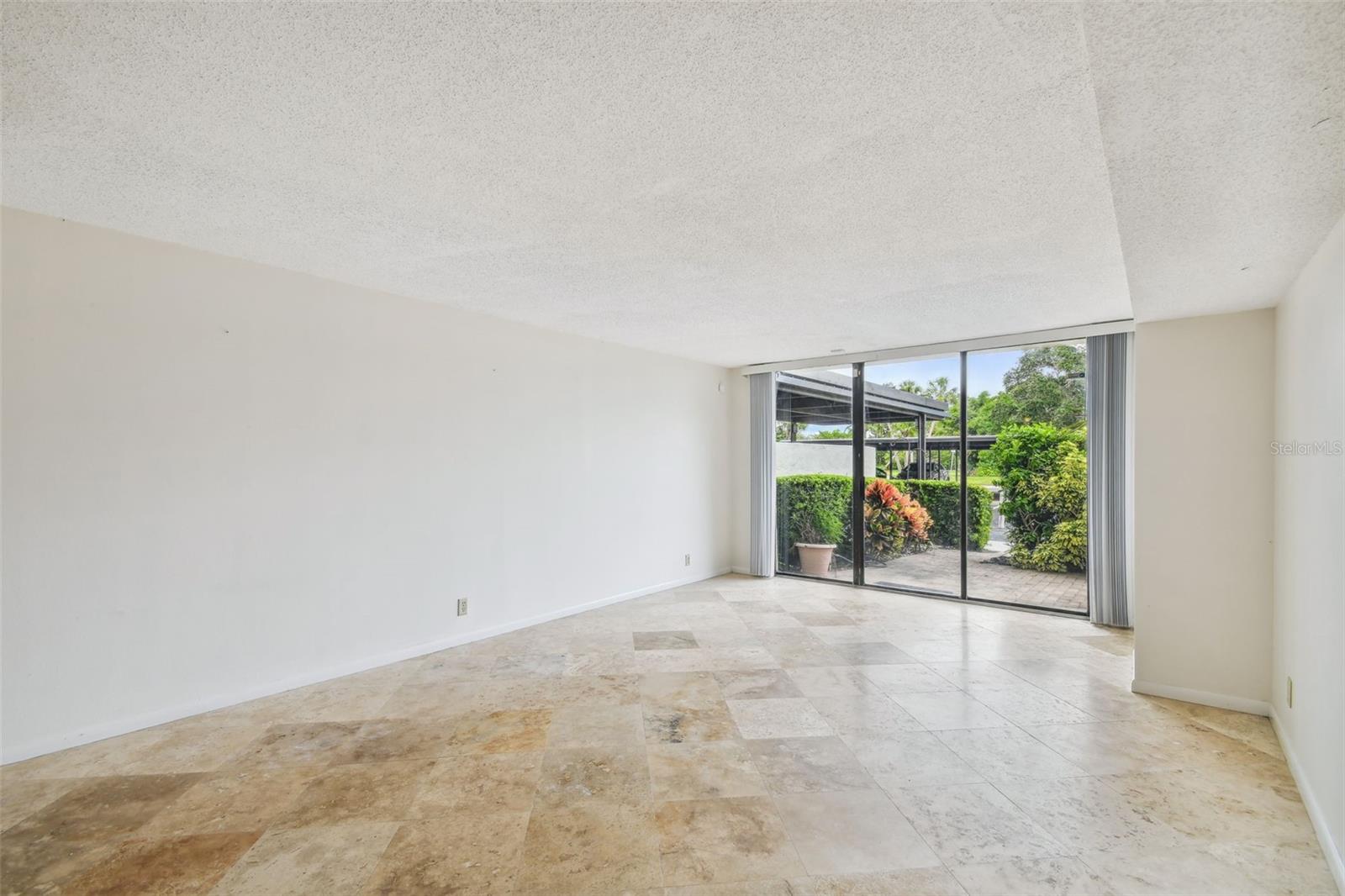 Vacant living room with stone tile floors and sliding glass doors opening to a landscaped patio.