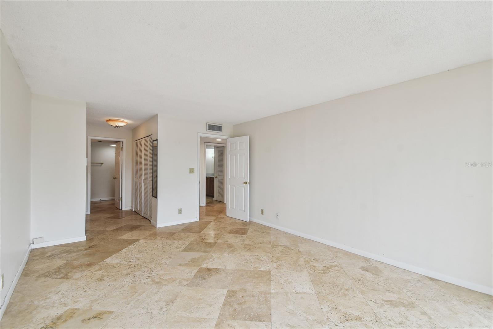 Vacant room with beige stone tile floors, louvered closet doors, and an open doorway.