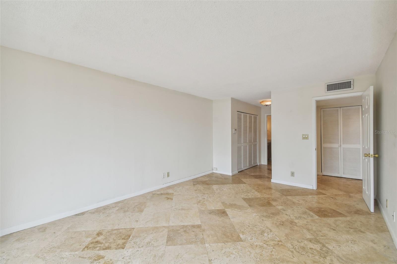 Vacant room with beige stone tile flooring, white walls, and louvered closet doors.
