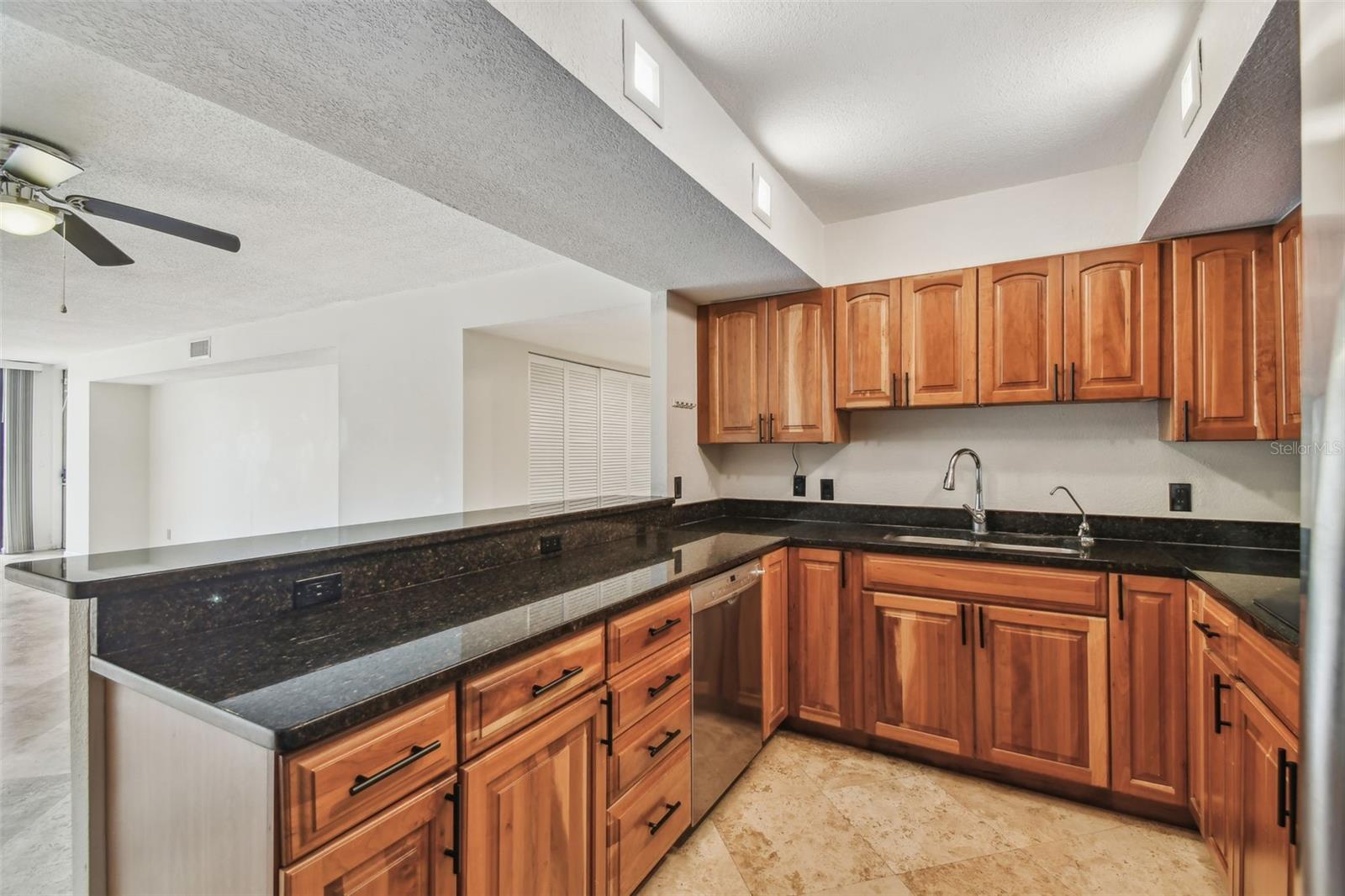 Kitchen with warm wood cabinets, dark granite counters, and a long breakfast bar.
