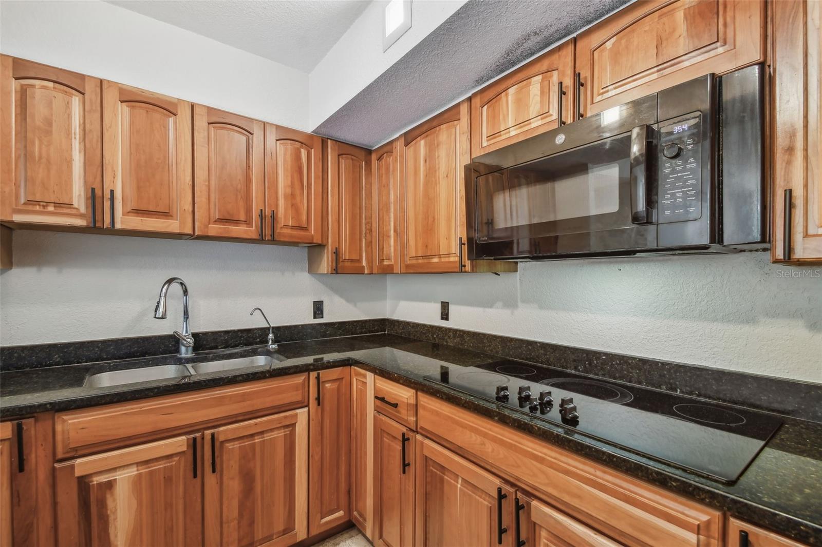 Kitchen with warm wood cabinets, dark countertops, a sink, and an electric cooktop.