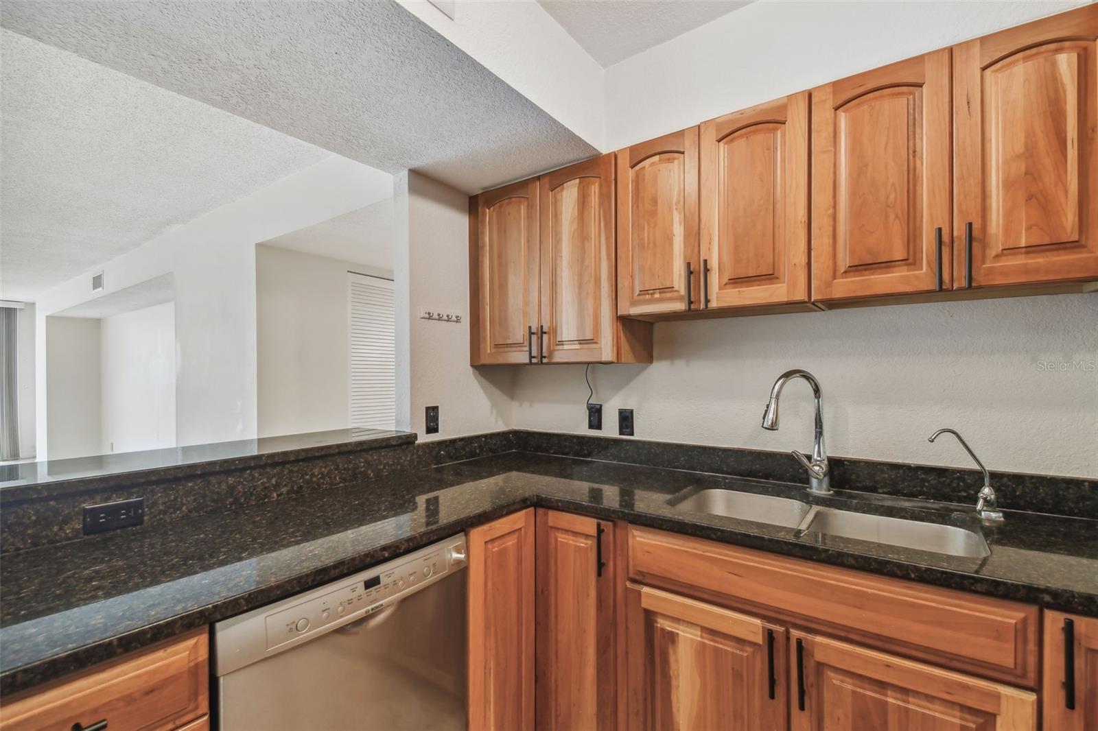 Kitchen with cherry-toned cabinets, dark counters, and a double-basin sink.