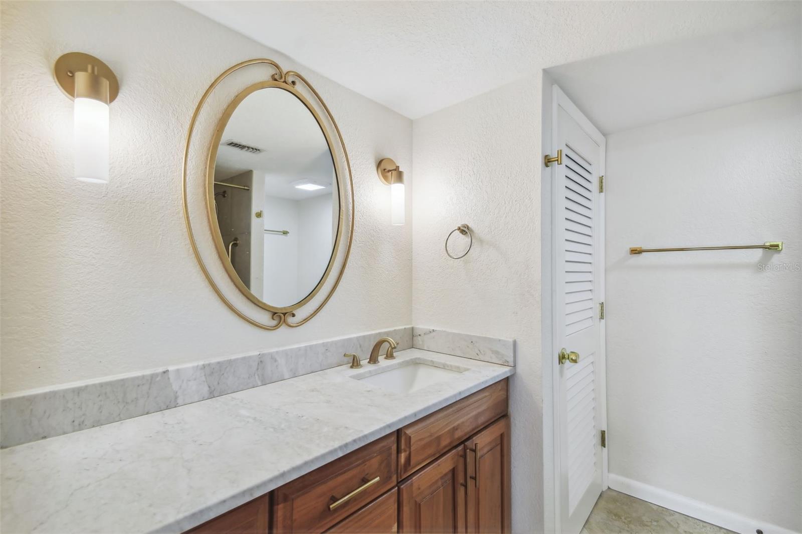 Bathroom vanity with a marble countertop, oval mirror, brass fixtures, and wood cabinetry.