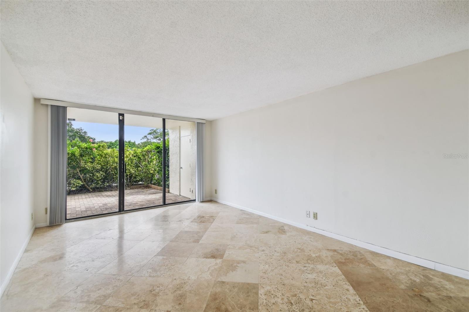 Empty living room with stone tile flooring and sliding glass doors to a paved patio.