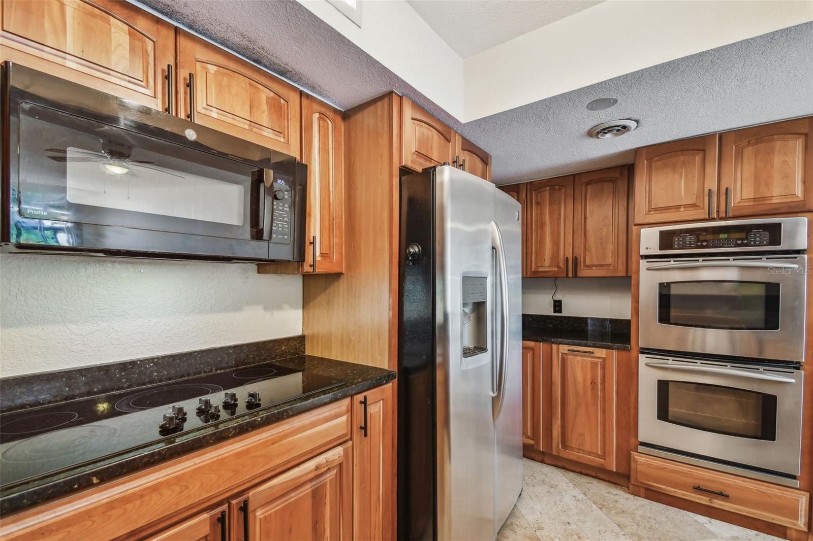 Kitchen with honey-toned wood cabinets, stainless steel appliances, and dark stone countertops.
