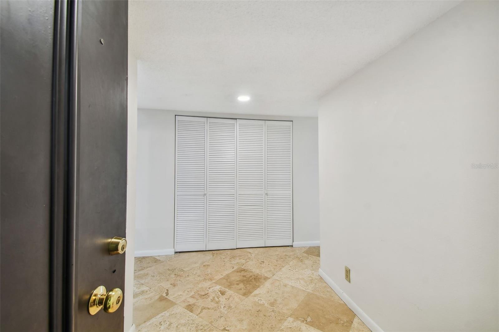 Entryway with beige stone tile flooring and white louvered closet doors.