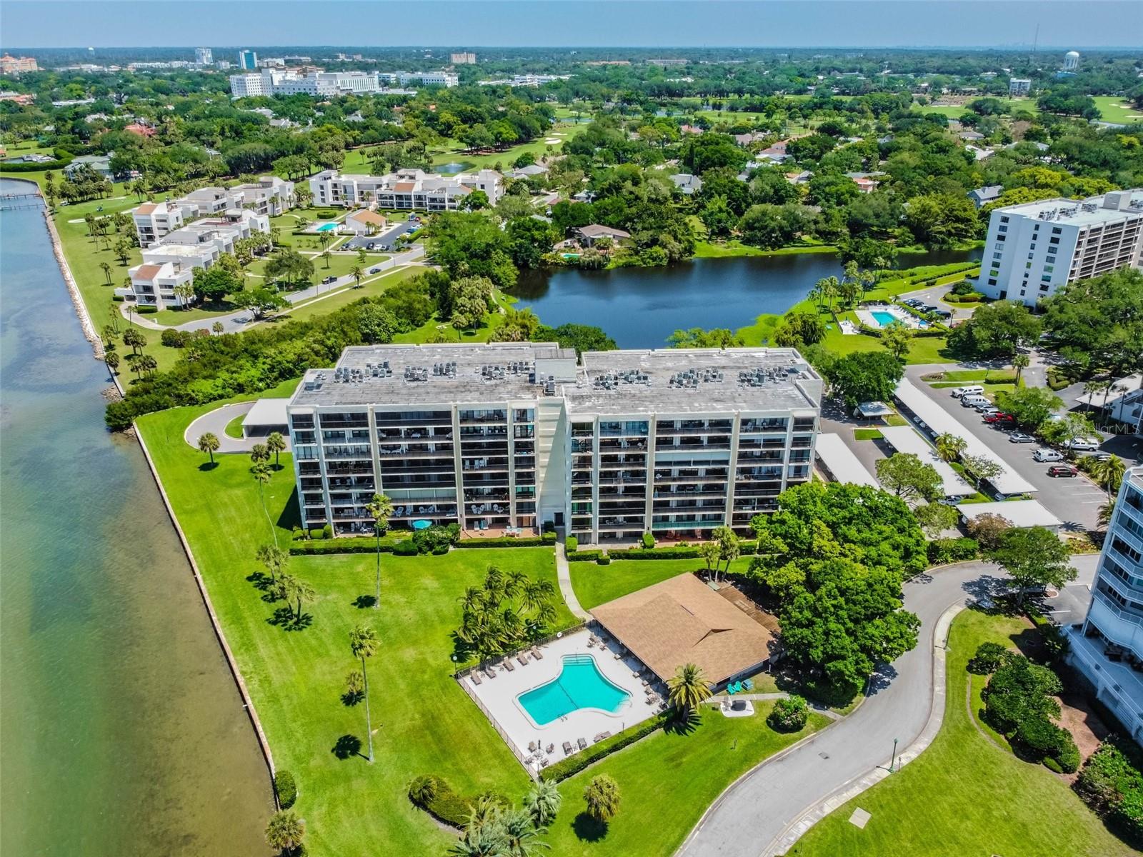 Aerial view of a waterfront condominium building with a pool, landscaped grounds, and a lake.