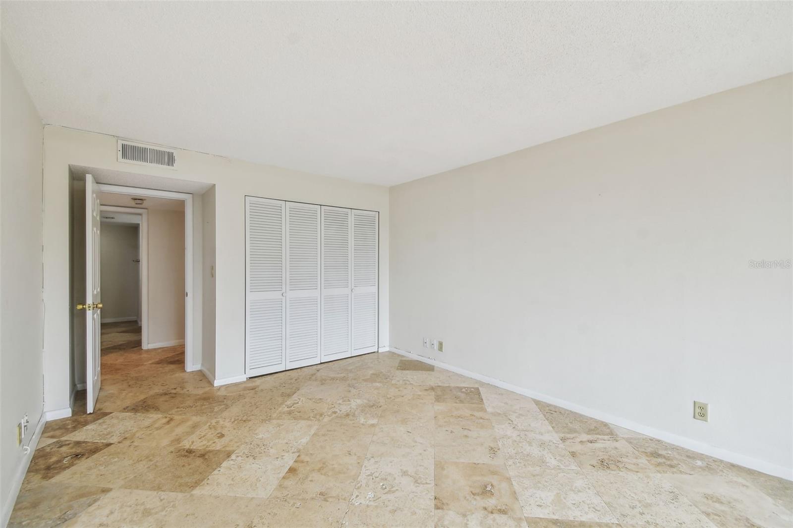 Vacant room with stone tile flooring, louvered closet doors, and an open doorway.