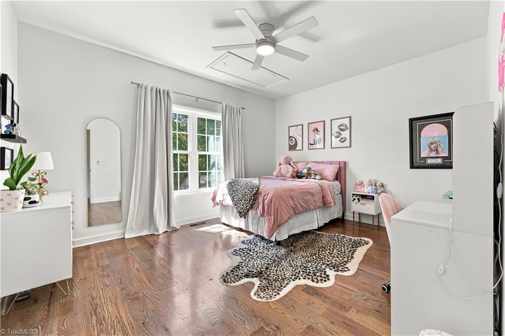 Furnished bedroom with a pink bed, hardwood floors, large windows, and an animal-print rug.