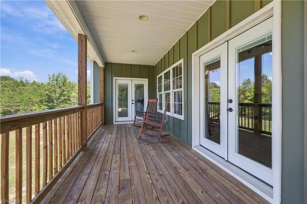 Covered wooden porch with green siding, white-framed glass doors, and two rocking chairs.