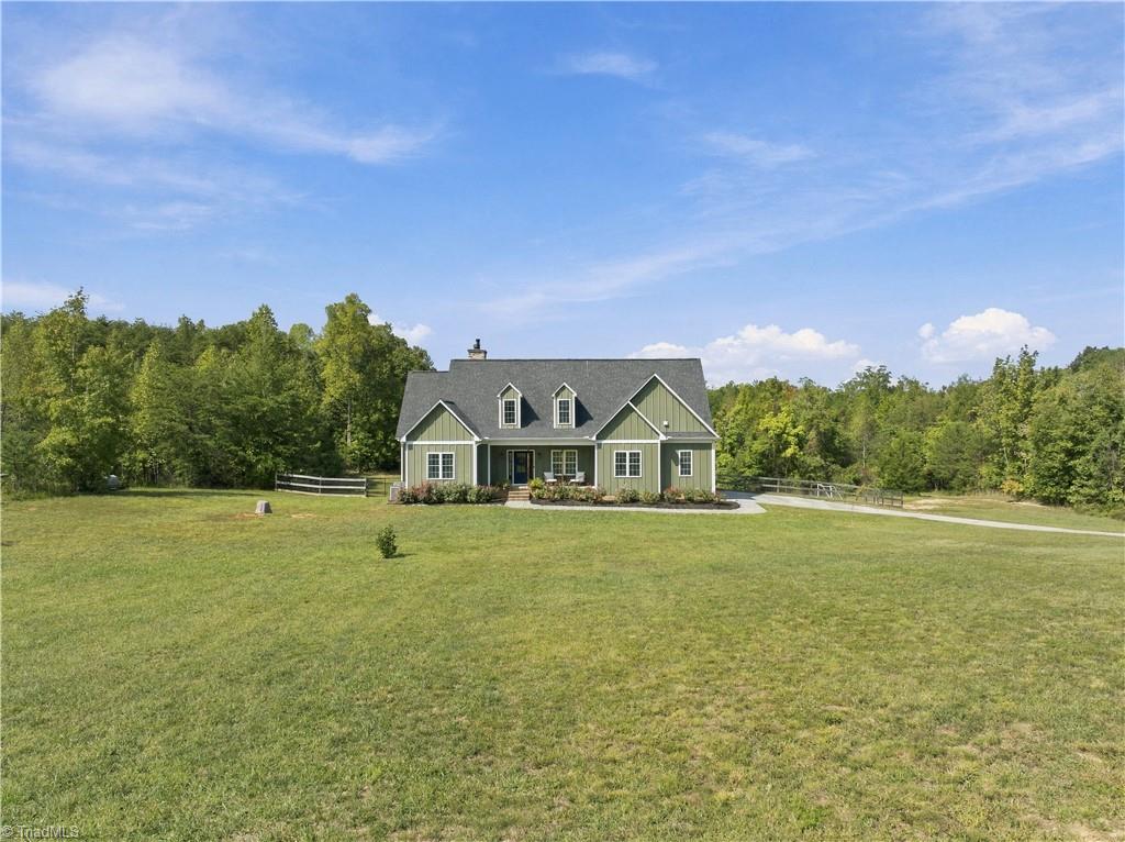 Green gabled home beyond a broad lawn, with woods behind it and a curved driveway.