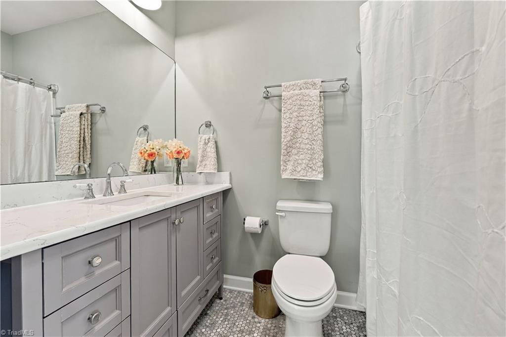 Bathroom with a gray vanity, white countertop, large mirror, and mosaic tile floor.