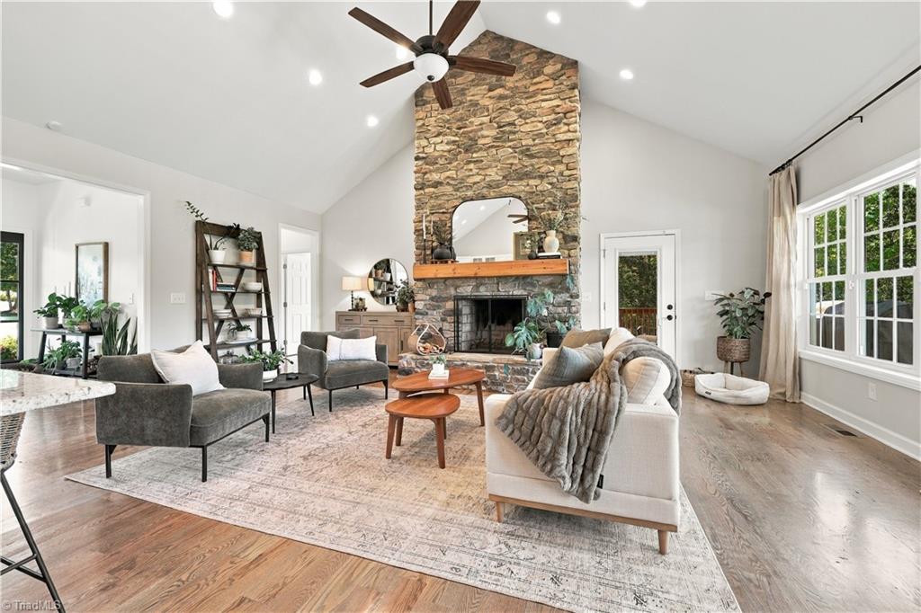 Staged living room with a tall stone fireplace, vaulted ceiling, and large windows.