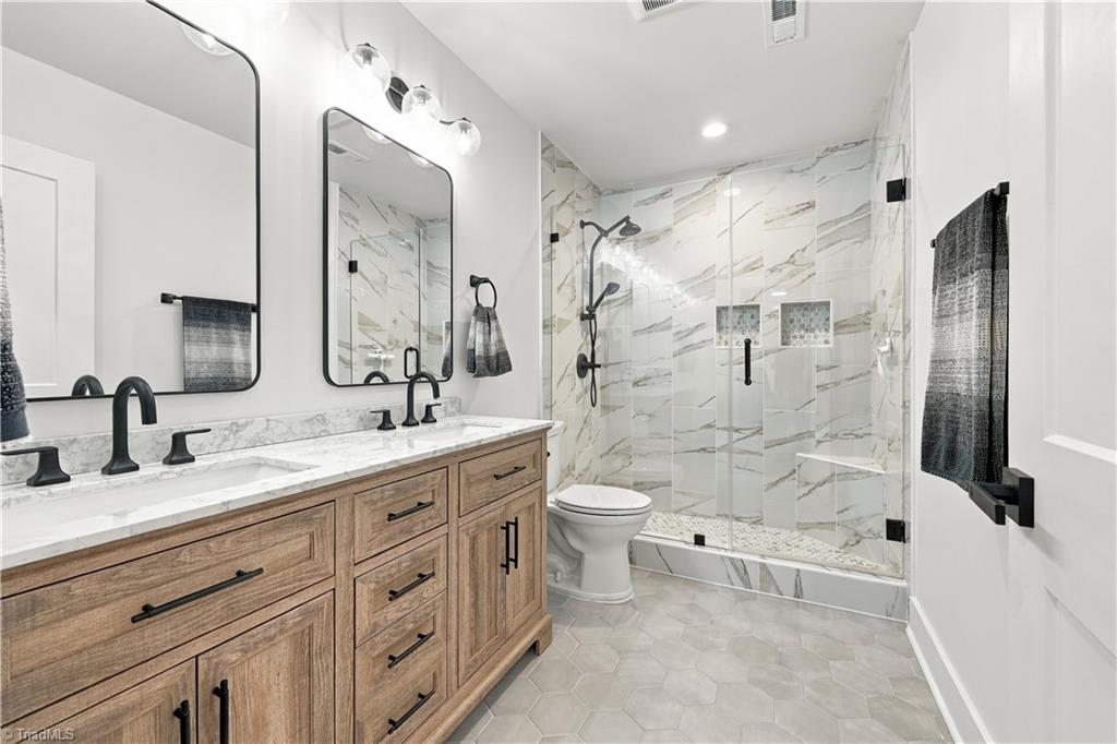 Bathroom with a wood double vanity and glass shower lined in marble-look tile.