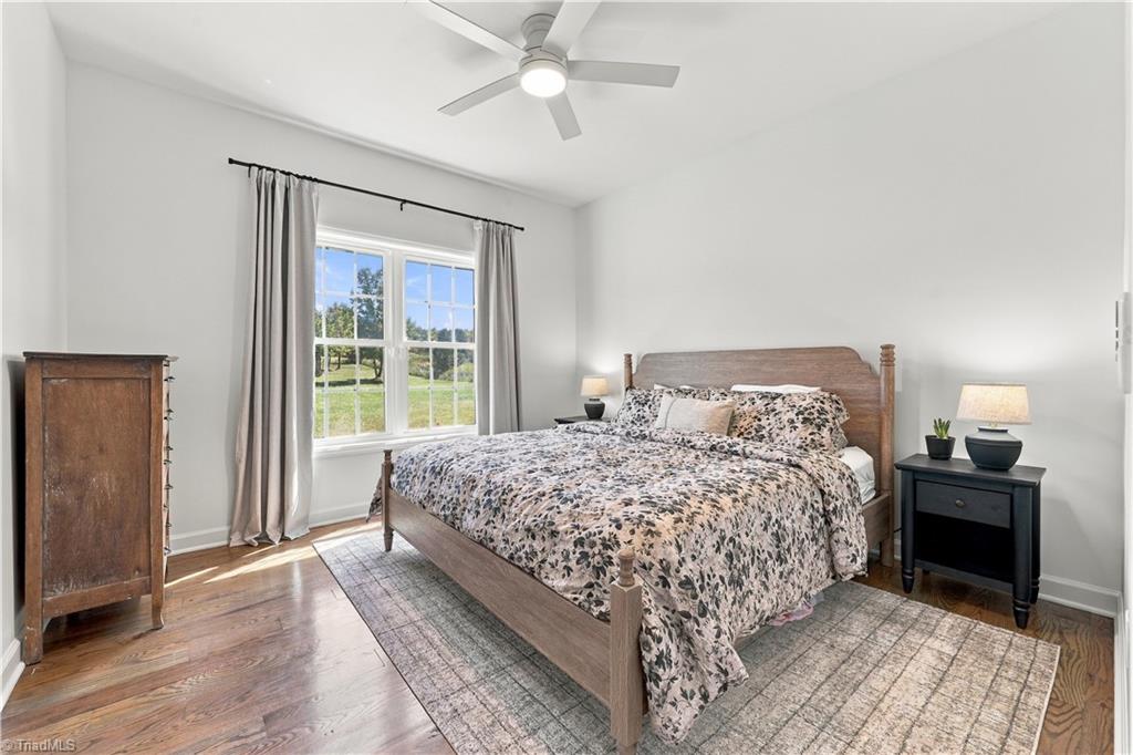 Furnished bedroom with floral bedding, a wooden bed, and a large window overlooking a lawn.