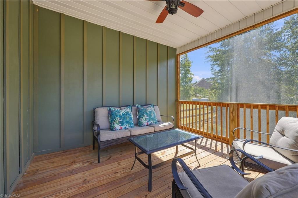 Screened porch with cushioned seating, a glass-top table, ceiling fan, and wood flooring.
