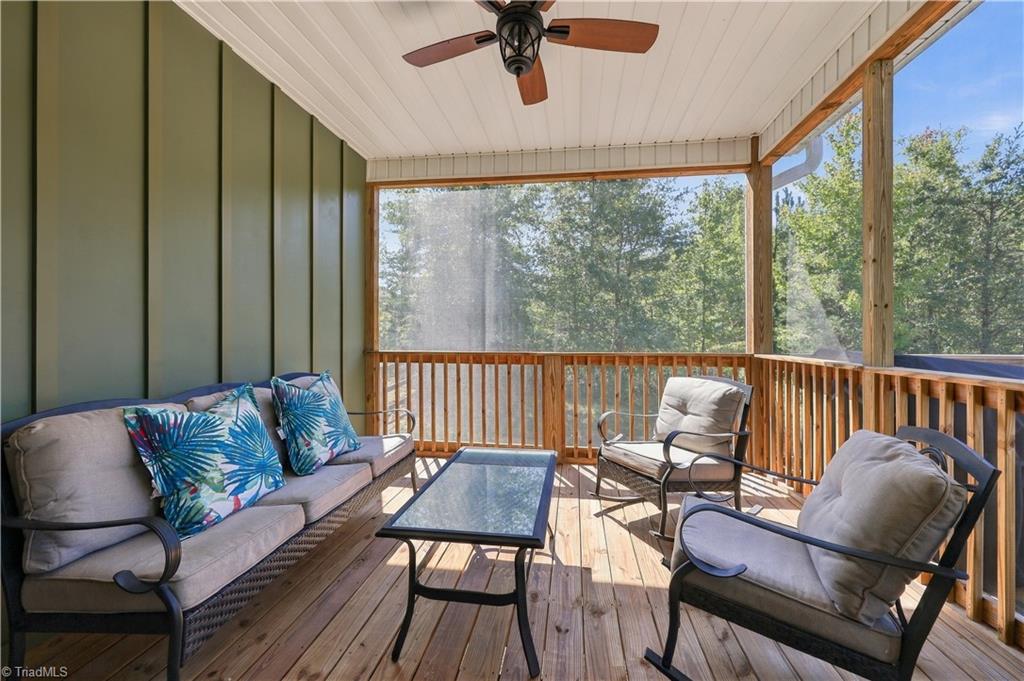 Screened porch with cushioned seating, a glass-top table, and a leafy wooded view.