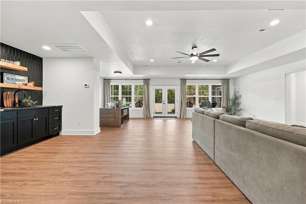 Open-plan living room with a gray sectional, black bar cabinet, and glass doors to the backyard.