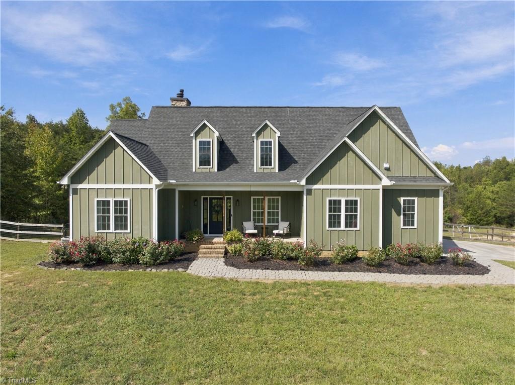 Green-sided house with two dormers, a covered porch, landscaped beds, and a broad front lawn.