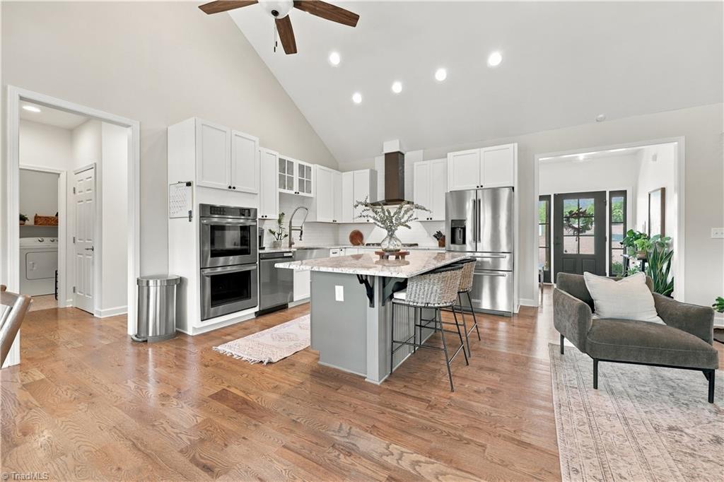 Kitchen with white cabinets, stainless appliances, a large island, and hardwood floors opening to a sitting area.