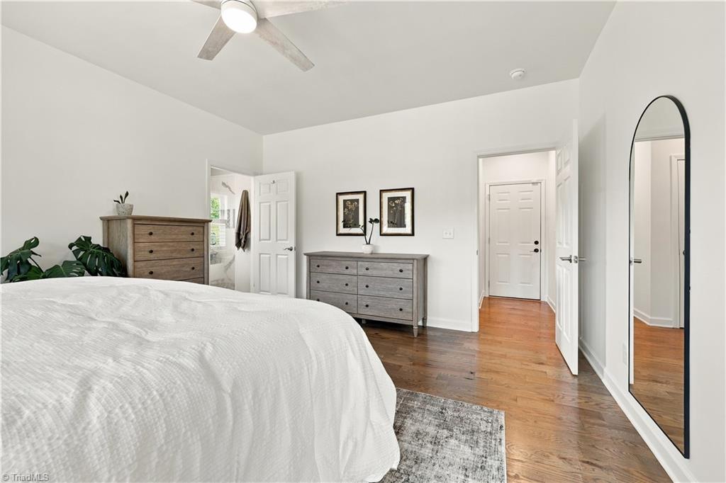 Bedroom with a white bed, wood dressers, hardwood floors, and a tall arched mirror.
