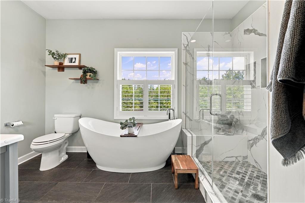 Bathroom with a freestanding soaking tub beneath a window and a glass-enclosed tile shower.