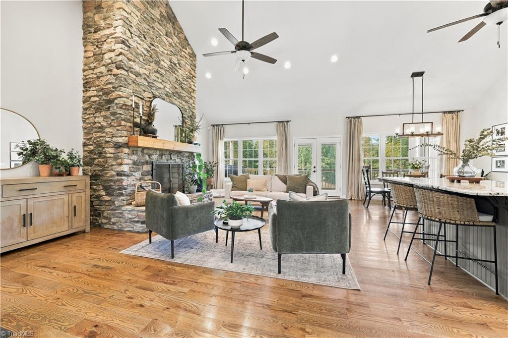 Open-plan living room with a tall stone fireplace, hardwood floors, and adjoining dining area.