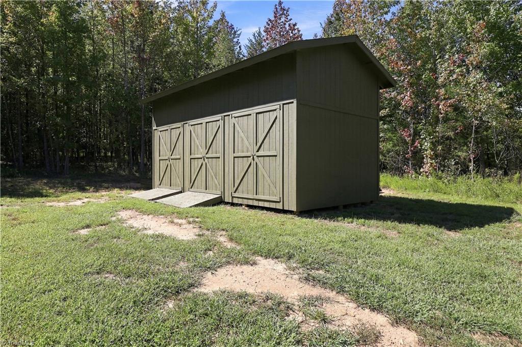 Olive-green storage shed with three barn-style doors in a grassy, wooded clearing.