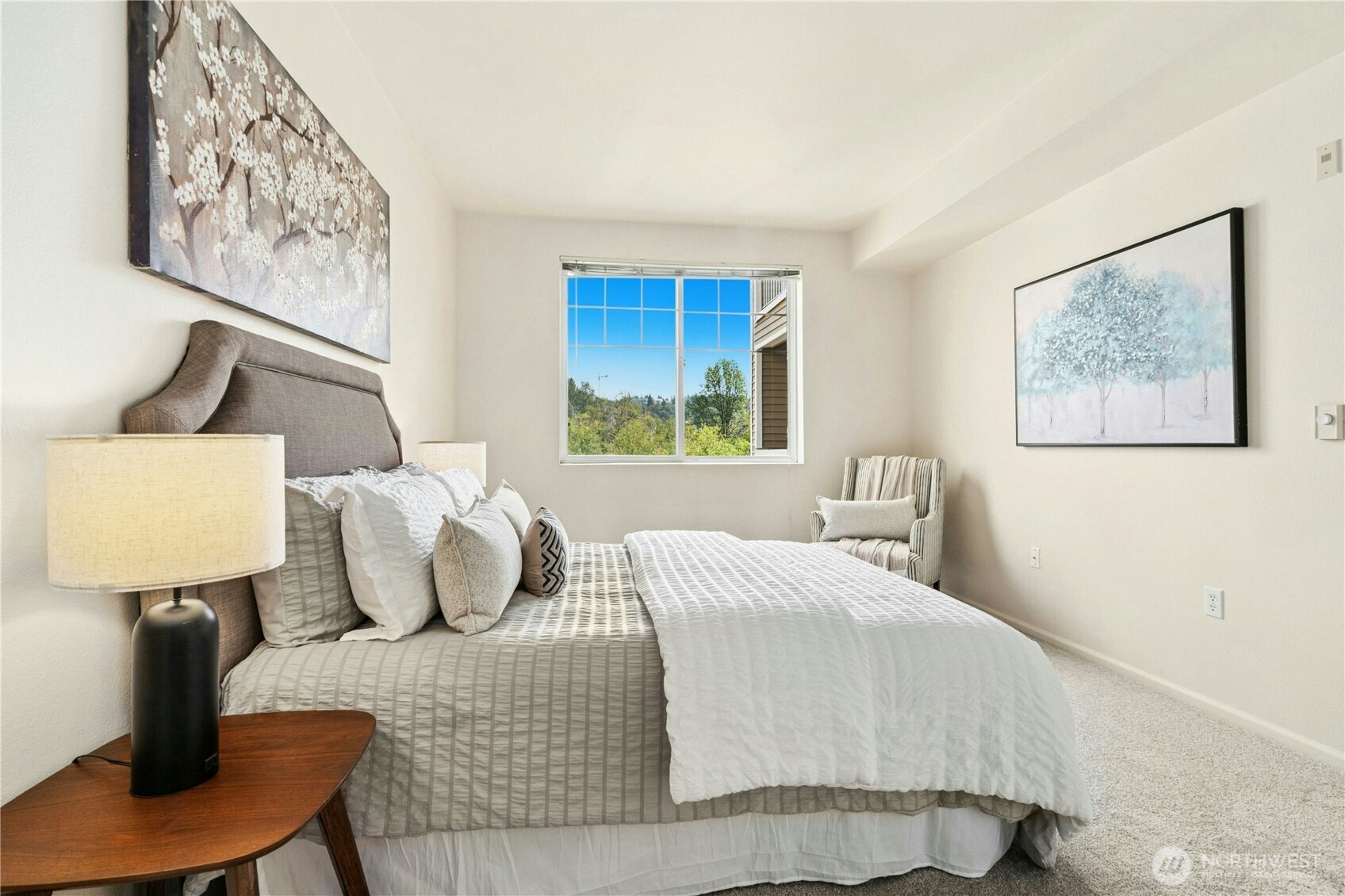 Furnished bedroom with a neatly made bed and a window overlooking trees.