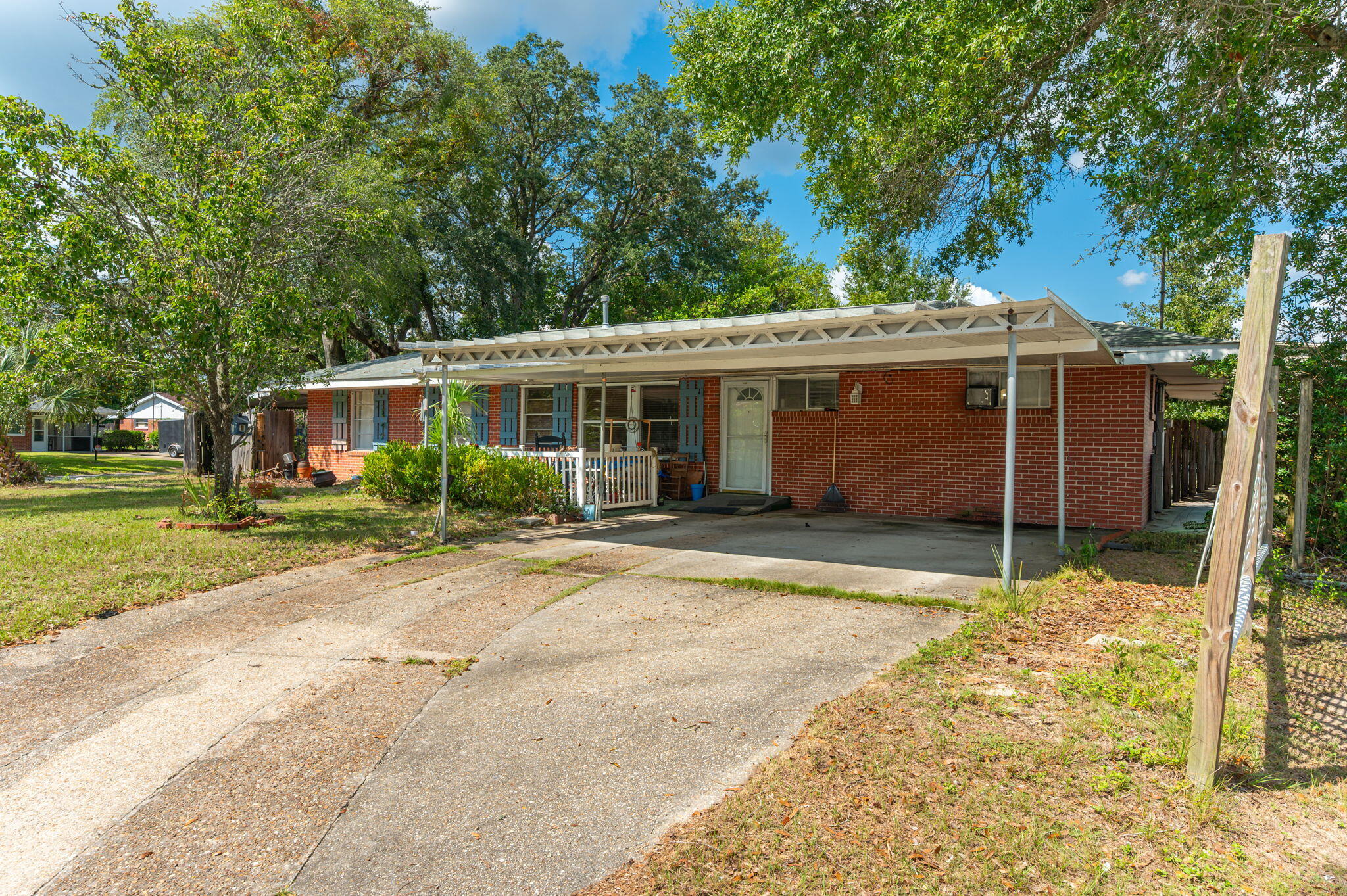 Red-brick ranch house with blue shutters, a wide white carport, and a concrete driveway.