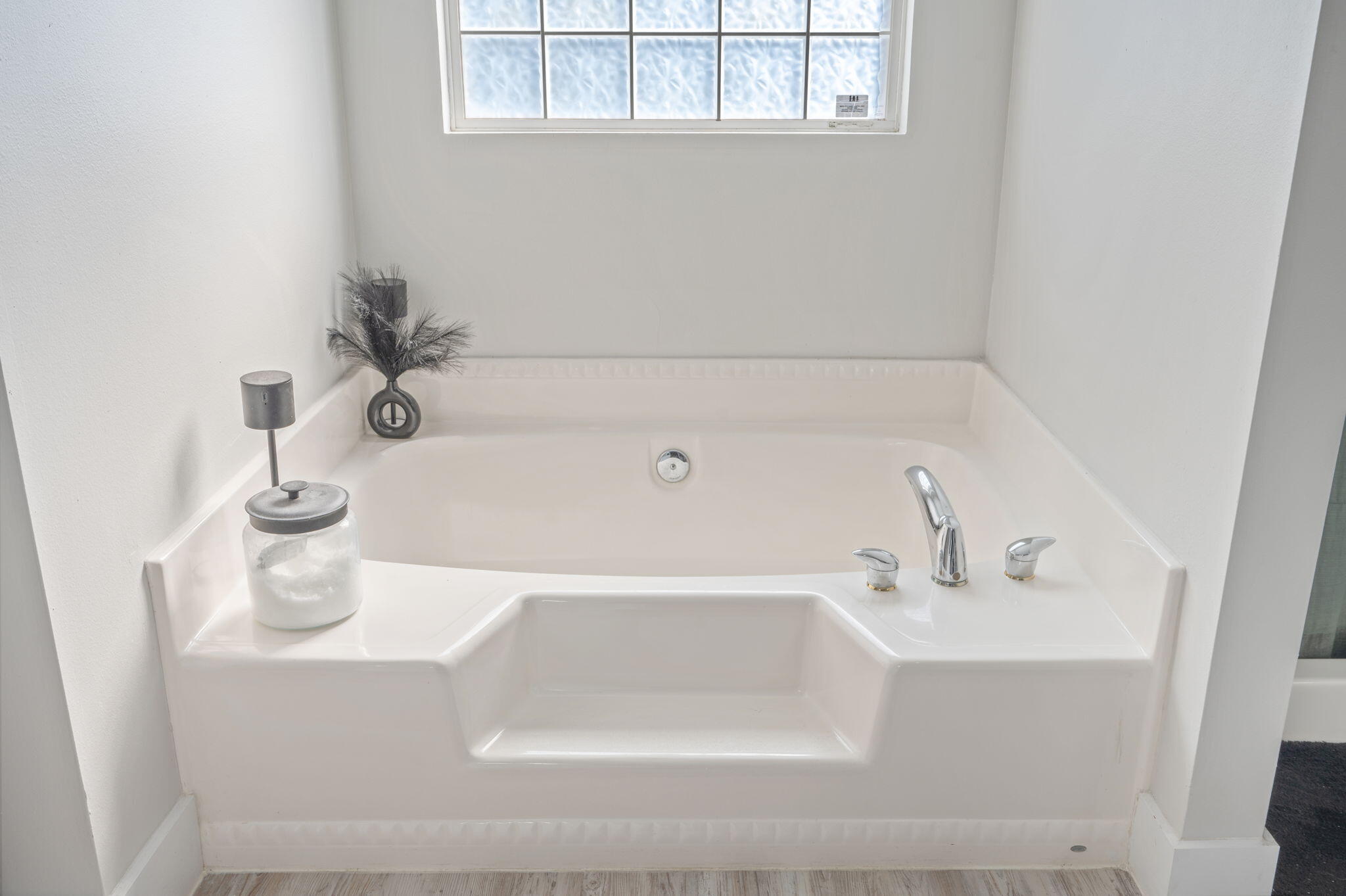Built-in bathroom soaking tub with chrome fixtures beneath a high window.